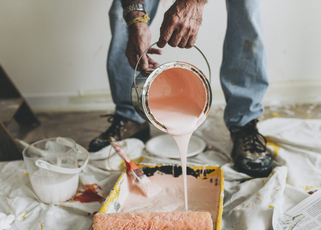 Man pouring white paint into a paint tin | Seasonal Shed Maintenance | Rooster's Amish Sheds, WV
