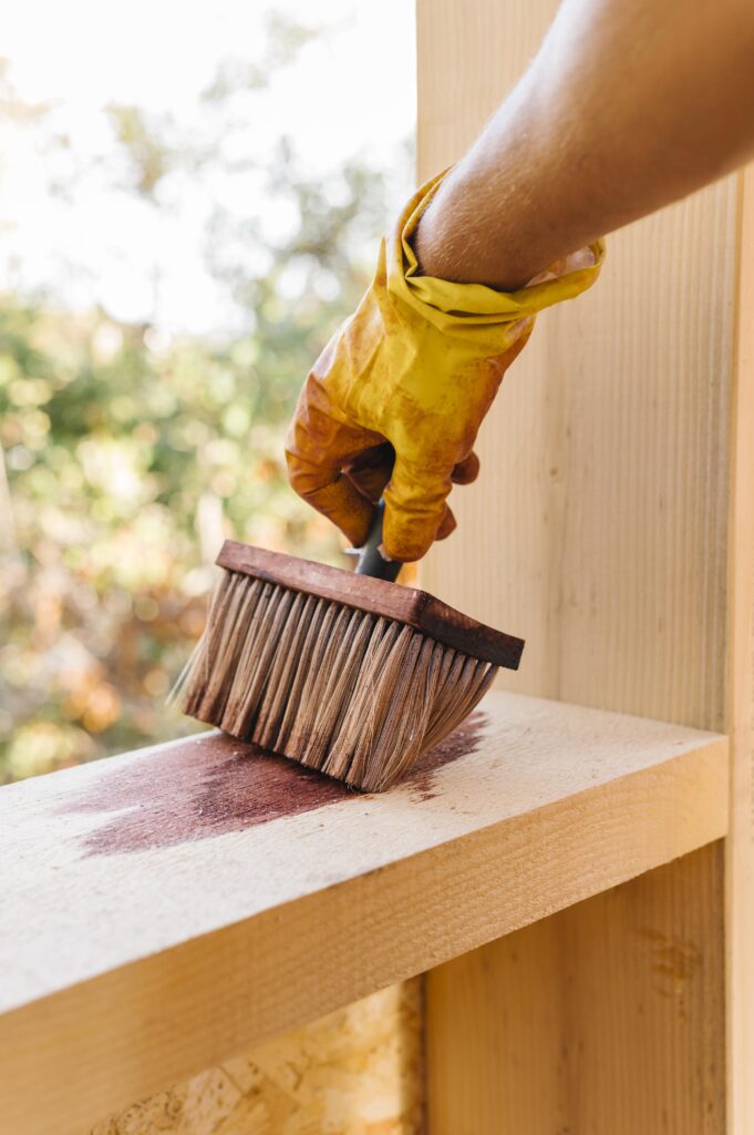 person varnishing piece wood from house construction | Weatherproofing Outdoor Structures | Rooster's Amish Sheds, WV