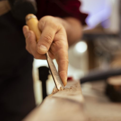 Handyman carving wood using chisel and hammer in carpentry shop, enjoying diy hobby. Man using traditional crafting process to shape wooden pieces with tools, making wood art, close up shot
