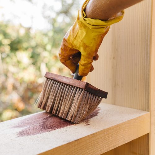 person varnishing piece wood from house construction | Weatherproofing Outdoor Structures | Rooster's Amish Sheds, WV