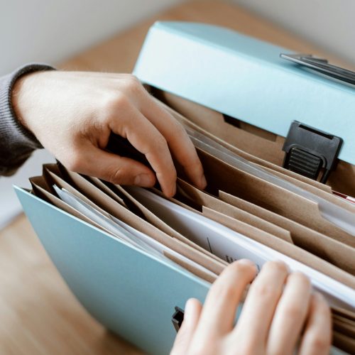 Filing cabinet filled with paperwork with a person's hands leafing through | Permits for Storage Building | Rooster's Amish Sheds, WV